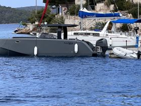 A sleek yacht docked in a picturesque harbor, showcasing its modern design against a scenic backdrop of lush greenery.