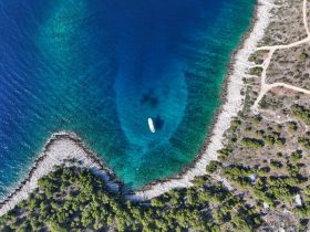 Aerial view of a boat navigating through crystal-clear waters, surrounded by a picturesque coastline and lush greenery — ideal for exploring secluded bays.