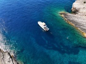 A stunning aerial view of a boat anchored near rocky shores, with snorkelers enjoying the crystal-clear waters — a perfect scene for adventure seekers.