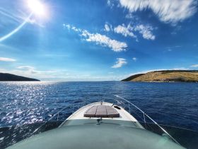 A stunning view from the front of a yacht cruising through sparkling blue waters, showcasing the beauty of the surrounding coastline and clear skies.