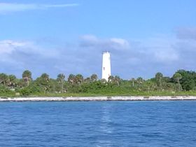 A picturesque view of a lighthouse standing tall against a backdrop of lush greenery and blue skies, perfect for capturing coastal landmarks during boating adventures.