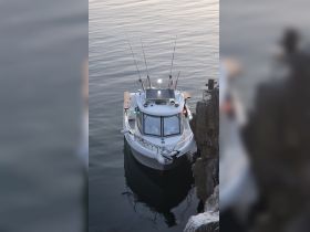 A fishing boat is docked peacefully, showcasing its sleek design and fishing gear, perfect for a day out on the water.