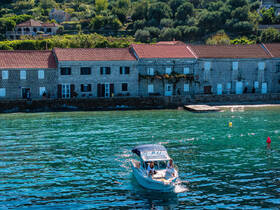 A charming scene of a boat navigating through clear waters near a picturesque coastline, with people enjoying the vibrant atmosphere along the shore.