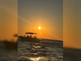 A silhouette of a boat with passengers cruising at sunset, creating a picturesque scene on the water — perfect for evening adventures.