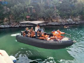 A lively group enjoys a boat ride in life jackets, with swimmers visible in the background — a perfect day for water adventures.