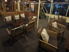 Cozy seating area inside a boat, featuring comfortable chairs and a warm wooden ambiance, perfect for relaxing during a cruise.
