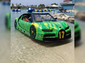 An unconventional vehicle resembling a car is partially submerged in shallow water, showcasing a vibrant design. The scene features a unique blend of land and water elements.