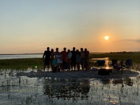 A group of friends gathers on a sandbar at sunset, enjoying a memorable celebration with scenic views — perfect for summer outings and beach adventures.