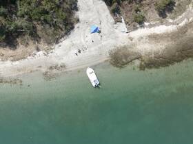 Aerial view of a boat docked on a serene beach, surrounded by clear waters and lush greenery — perfect for a day of relaxation and exploration.