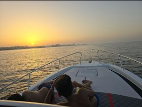 Two children relax on the bow of a boat, enjoying a stunning sunset over the water — a perfect moment for family bonding on the sea.