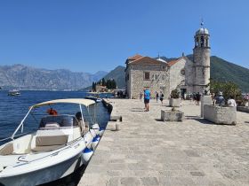 A picturesque scene featuring a small boat docked near a historic church, with visitors enjoying the stunning coastal views in the background — a perfect spot for sightseeing in Montenegro.