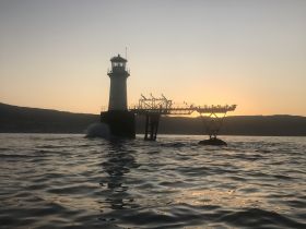 A silhouette of a lighthouse against a sunset backdrop, capturing a serene moment on the water.
