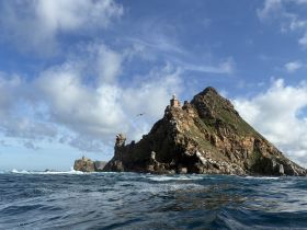 A stunning view of a rocky island with a lighthouse, surrounded by crashing waves and dramatic skies — a perfect representation of coastal beauty.