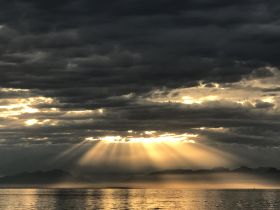 A stunning sunset casts rays of light through the clouds over tranquil waters, creating a picturesque scene perfect for nature lovers and photographers.