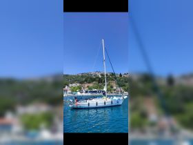 A beautiful sailboat named 'ARGO' docked in calm waters, surrounded by picturesque hills and charming coastal homes.