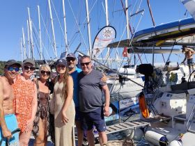 A cheerful group of friends poses for a photo on the dock, celebrating their sailing adventure together. The vibrant atmosphere captures the joy of a day spent on the water.