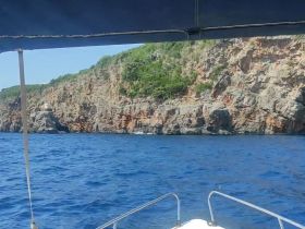 A stunning view of rocky cliffs and clear blue waters from the deck of a boat, showcasing the natural beauty of the coastline.