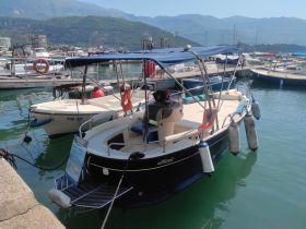 A sleek boat docked in a marina, showcasing its elegant design against a backdrop of mountains and other vessels — perfect for exploring coastal waters.
