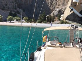 A serene view of a sailboat anchored in crystal-clear waters, with a picturesque beach and rocky cliffs in the background, perfect for exploring secluded destinations.