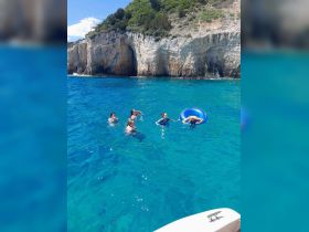 A lively group enjoys a refreshing swim in the stunning blue waters, surrounded by beautiful cliffs — a perfect day of fun and relaxation on the water.