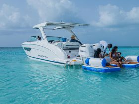 A lively group enjoys a fun day on the water, relaxing on a pontoon and interacting with a stylish boat in the background — perfect for summer adventures.