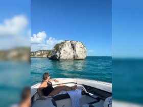 A woman relaxes on the deck of a boat, enjoying the stunning view of a rocky island in the turquoise waters — a perfect moment for leisure and exploration.