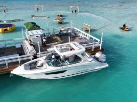 A vibrant scene at a dock with a boat and jet ski, showcasing people enjoying water activities in the stunning turquoise waters.