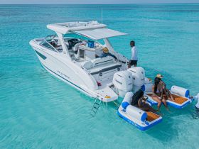 A lively group enjoys a fun day on the water, relaxing on inflatable mats beside a sleek boat in crystal-clear turquoise waters.
