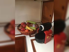 A cozy kitchen setup on a boat featuring a basket of fresh fruits and a coffee machine, perfect for enjoying snacks and beverages while at sea.