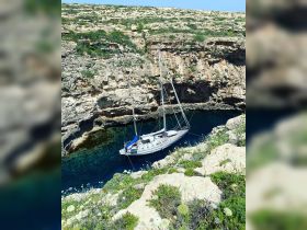 A stunning aerial view of a sailboat anchored in a secluded cove, surrounded by rocky cliffs and crystal-clear turquoise waters, perfect for serene getaways.