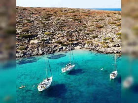 A stunning aerial view of sailboats anchored in a crystal-clear bay, with guests enjoying swimming and kayaking — a perfect getaway for water enthusiasts.