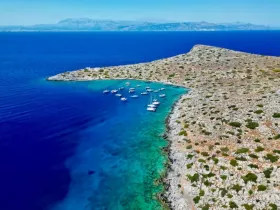 A stunning aerial view of a serene coastline with multiple boats anchored in turquoise waters, showcasing the natural beauty of the landscape.
