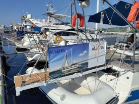 A detailed view of the yacht 'Albena' docked at the marina, showcasing its structure and branding against a clear blue sky.