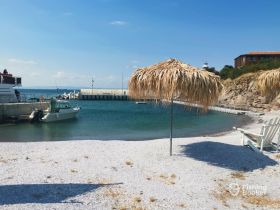 A serene view of a small boat docked at a picturesque harbor, surrounded by clear waters and a sandy beach — perfect for a relaxing day by the sea.
