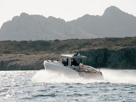 A sleek speedboat navigates through sparkling waters, showcasing its dynamic design against a backdrop of rugged cliffs — perfect for thrilling adventures on the sea.