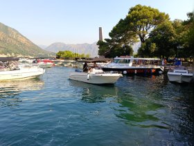 A bustling marina scene with various boats, including a motorboat tour, set against a stunning mountainous backdrop — perfect for exploring the coastline.