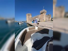 A view of the comfortable seating area inside a boat, showcasing a sleek design against a backdrop of a historic stone castle by the water.