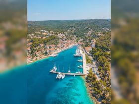 A stunning aerial view of a picturesque harbor surrounded by lush greenery and charming coastal homes, showcasing the beauty of the landscape and the vibrant blue waters.