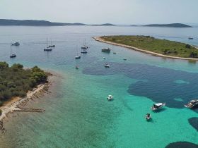 A stunning aerial view of multiple boats anchored in crystal-clear turquoise waters near a picturesque island, perfect for sailing adventures and exploring coastal beauty.
