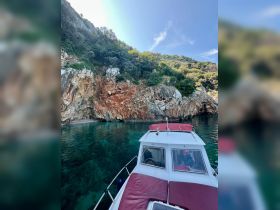 A scenic view of a boat anchored near a rocky coastline, showcasing the vibrant turquoise waters and lush greenery — perfect for exploring hidden coves and enjoying nature.