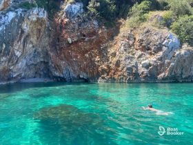 A swimmer enjoys the crystal-clear waters near a rocky coastline, capturing the essence of a perfect beach day in a secluded cove.