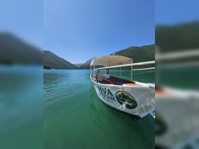 A picturesque view of the 'Piva Dream' boat gliding through serene turquoise waters, surrounded by lush green mountains — perfect for exploring scenic landscapes.