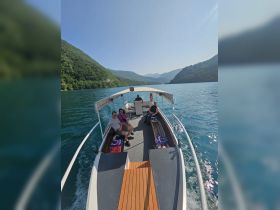 A group enjoys a scenic boat ride on a tranquil lake surrounded by lush mountains, perfect for exploring nature and creating memorable experiences.