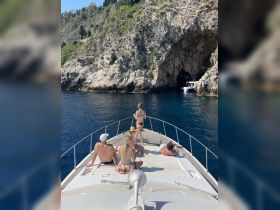 A lively group enjoys drinks on the deck of a boat while exploring a scenic coastal cave — perfect for summer adventures and memorable outings.