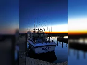 A serene sunset view of the fishing boat 'TOO EZ' docked at the marina, showcasing its multiple fishing rods against a vibrant sky.