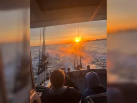 Guests enjoy a stunning sunset while fishing aboard a boat, capturing the perfect moment on camera — an ideal scene for fishing enthusiasts and sunset lovers.