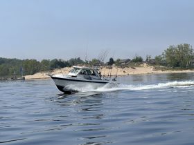 A sleek fishing boat speeds through calm waters, showcasing its design and fishing gear, perfect for a day on the lake.