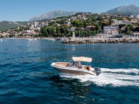 A sleek speedboat glides through clear waters, showcasing a picturesque coastal backdrop — perfect for exploring the stunning shoreline.