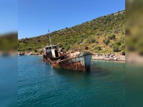 A striking view of a rusty, abandoned shipwreck partially submerged in tranquil waters, surrounded by lush greenery — a haunting reminder of maritime history.