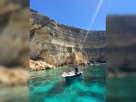 A joyful group enjoys a sunny day on a boat amidst stunning turquoise waters and dramatic cliffs, perfect for exploring coastal beauty.